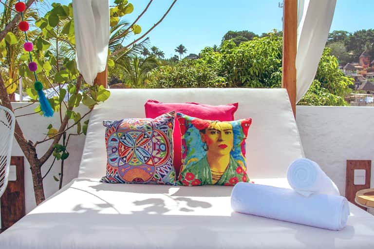 White bed with colorful decorative pillows on terrace overlooking tropical garden landscape