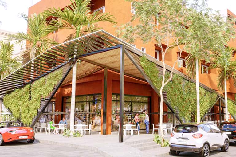 Modern resort entrance with living green wall, orange building, and parked vehicles