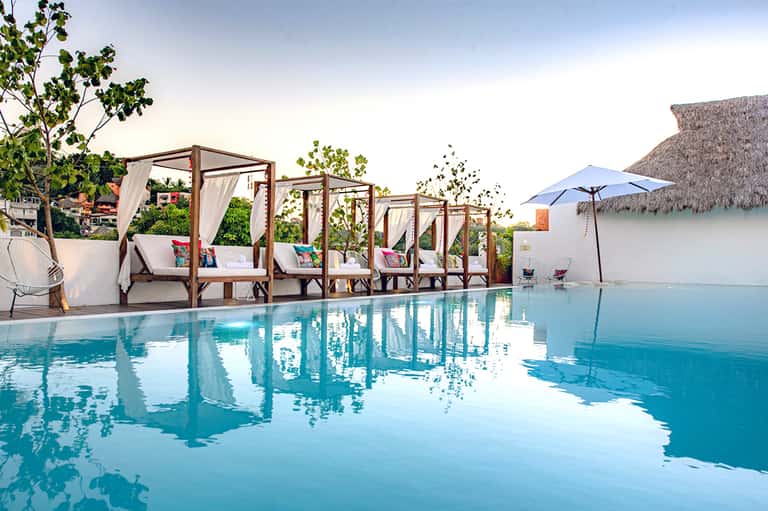 Luxury pool area with white canopy beds, palm trees, and modern architecture
