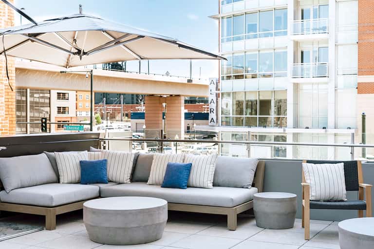 Rooftop lounge with gray sectional sofa, striped pillows, umbrellas, and waterfront skyline views