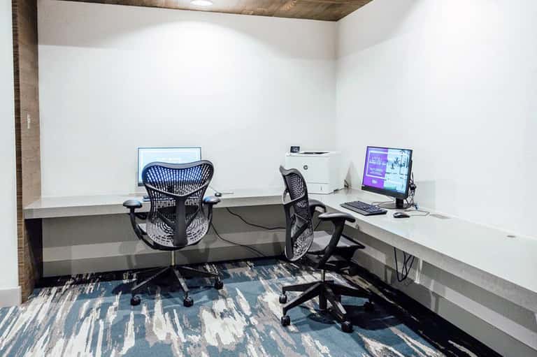 Modern business center with dual desk workstations, ergonomic chairs, and computer monitors