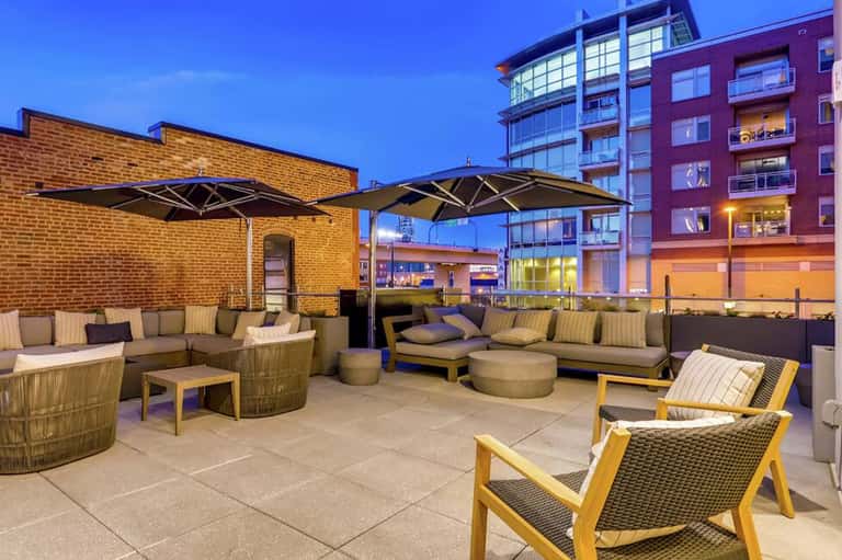 Urban rooftop lounge at dusk with woven seating, black umbrellas, and illuminated buildings in the background
