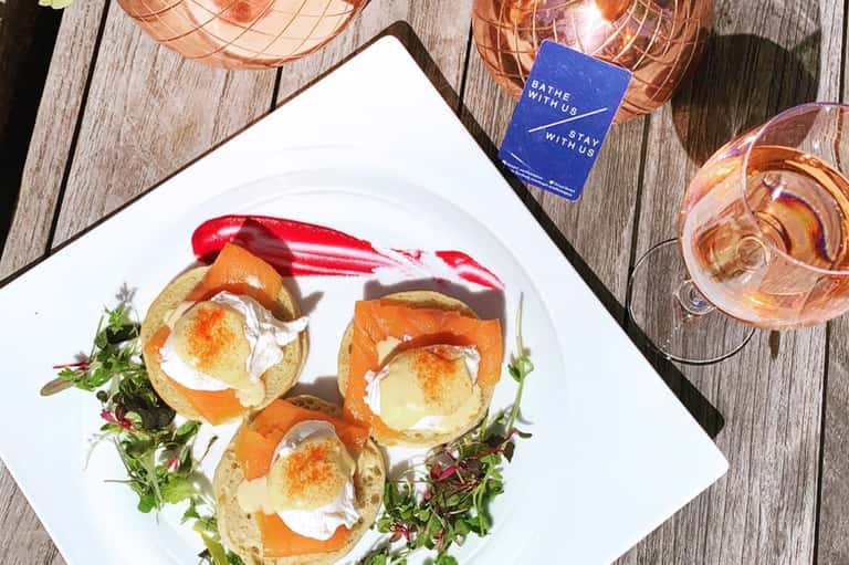 Appetizers with poached eggs on toast alongside rosé wine on wooden deck