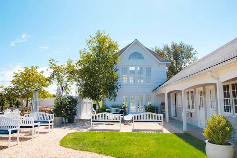 Coastal farmhouse with white architecture, wraparound porch, and manicured lawn