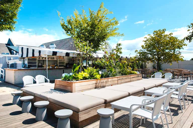Resort rooftop deck with casual seating, striped cabana, bar counter, and manicured landscaping