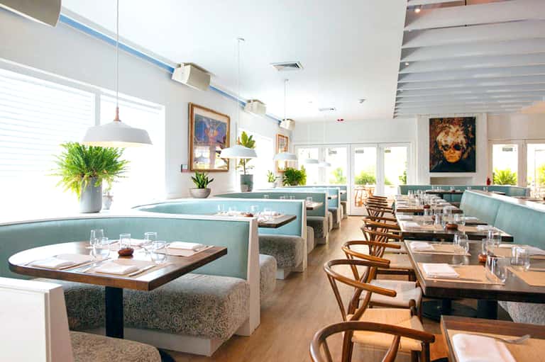 Modern restaurant interior with turquoise booth seating, wood chairs, pendant lights, and plant décor