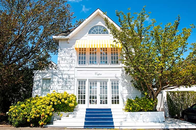 Charming white cottage-style building with yellow awning and yellow hydrangeas at entrance