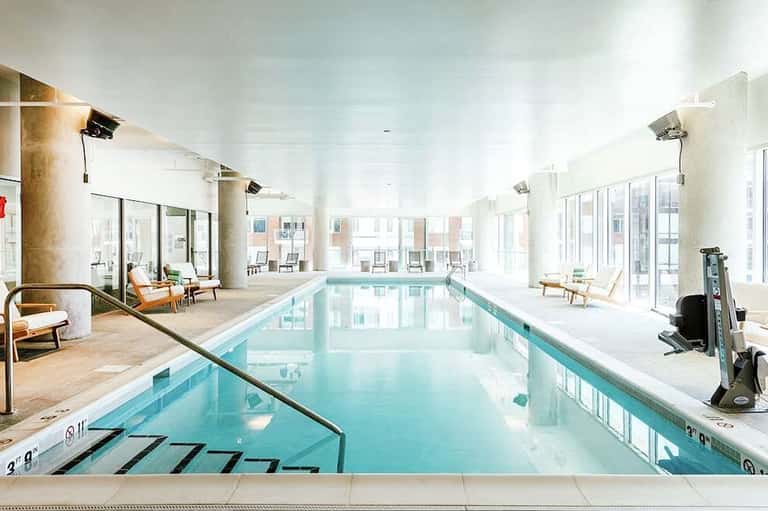 Indoor lap pool with bright natural lighting, lounge chairs, and modern amenities