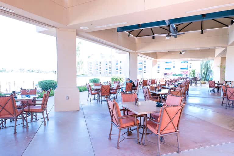 Covered outdoor dining area with coral chairs and tables overlooking waterfront and residential buildings