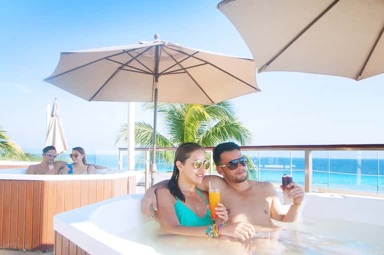 Couple relaxing in an outdoor hot tub with ocean view and umbrellas