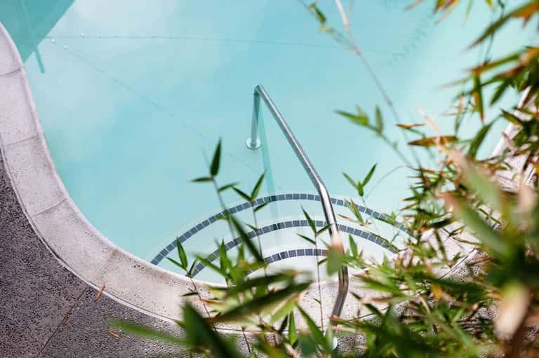 Spiral staircase railing reflected in bright turquoise pool water with landscaping in foreground