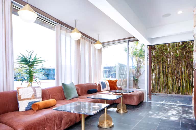 Modern lounge with coral sectional sofa, pendant lighting, floor-to-ceiling windows, views of cityscape and bamboo accent wall