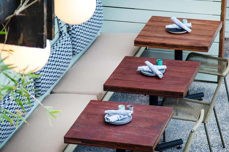 Outdoor dining tables with wood tops and patterned cushions set for service at beachfront resort