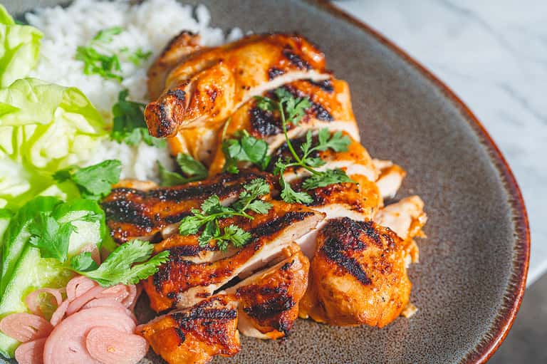 Roasted duck sliced and plated with jasmine rice, fresh herbs, and pink pickled vegetables