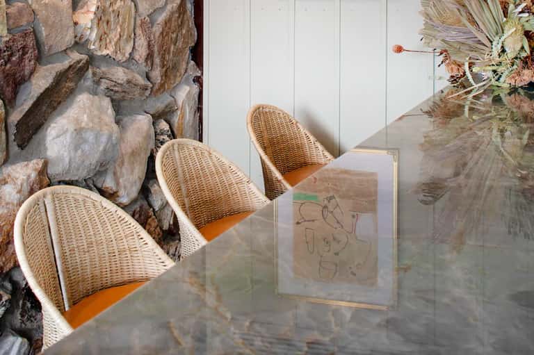 Wicker chairs on patio overlooking stone wall and tropical garden with dried plants