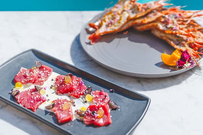 Gourmet seafood dish with decorative garnish and lobster on white and blue plates by pool