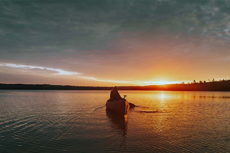 Kayaker paddling on calm water at sunset with golden sky reflection