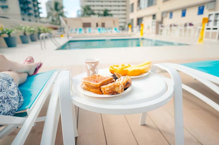 Poolside dining table with burger, fries, and beverage overlooking turquoise pool