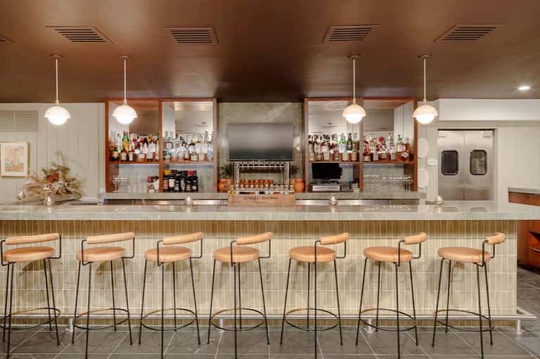 Modern hotel bar with wooden stools, pendant lighting, and stocked liquor shelves