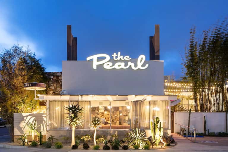 The Pearl restaurant entrance illuminated at dusk with modern signage and tropical landscaping