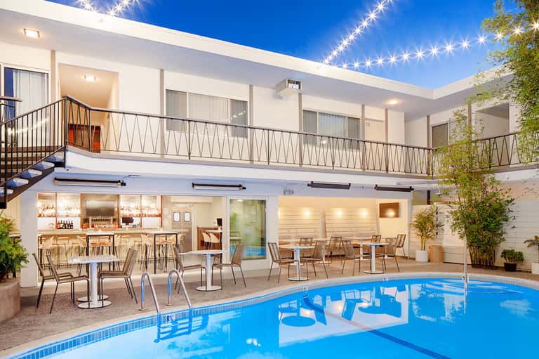 Contemporary pool area at night with illuminated terrace, bar, lounge chairs, and modern white building architecture