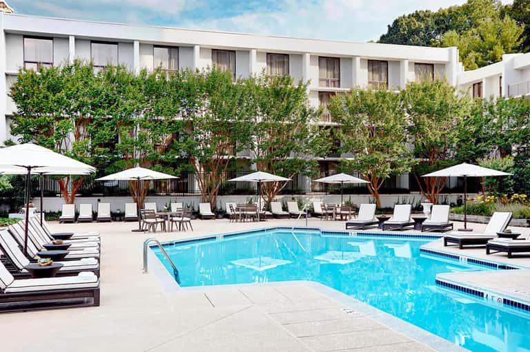 Resort pool with lounge chairs, white umbrellas, and ivy-covered building backdrop