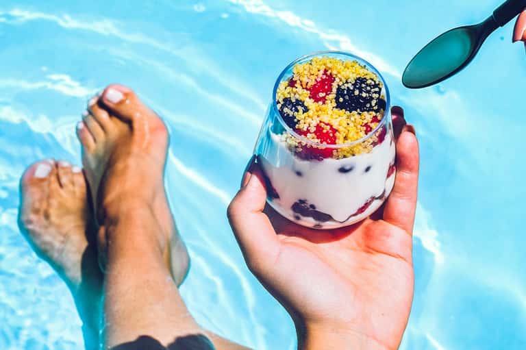 Close-up of colorful beverage with fruit cereal topping held above swimming pool water