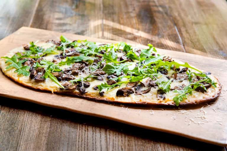 Gourmet flatbread pizza with arugula and mushrooms on wooden serving board