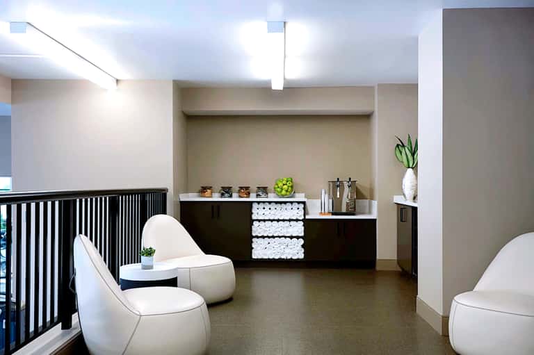 Modern spa reception area with minimalist design, white chairs, black accents, and neatly stacked towels