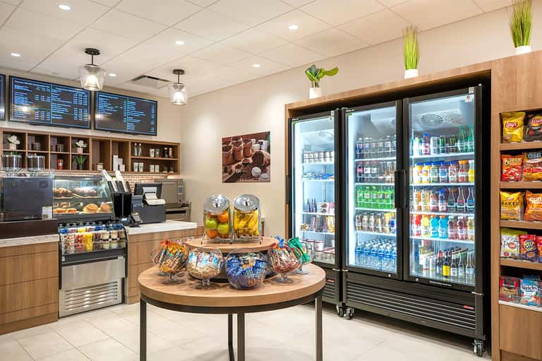 Modern hotel café interior with menu boards, coffee station, refrigerated beverages, and wooden accents