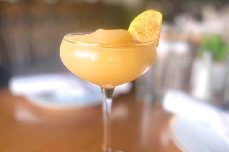 Golden cocktail drink with cinnamon chip garnish on blurred restaurant background