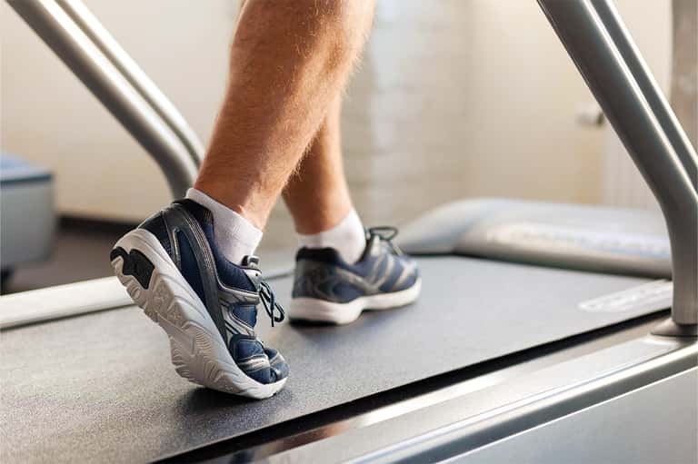 Man's feet in running shoes on a treadmill during a workout at a fitness center