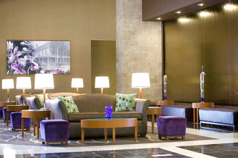 Modern hotel lobby lounge with gray sofa, purple ottomans, green accent pillows, and ambient lighting