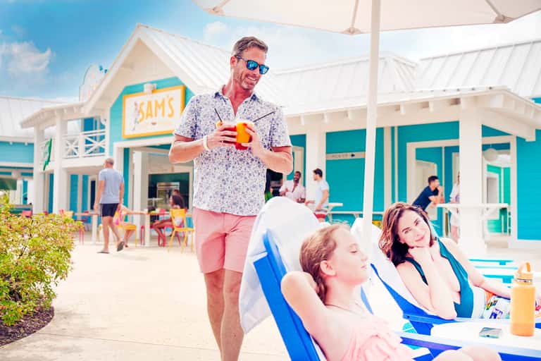 Family relaxing at beachfront bar with turquoise umbrellas and tropical buildings