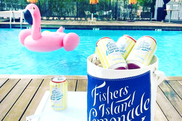 Poolside scene with pink flamingo float, beer cans, and wooden dock overlooking blue water