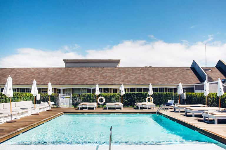 Resort outdoor swimming pool with turquoise water, white umbrellas, lounge chairs, and brick building backdrop