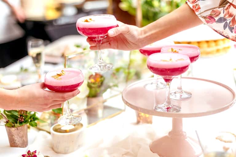 Woman holding vibrant pink cocktails at an outdoor dining event with fresh garnishes