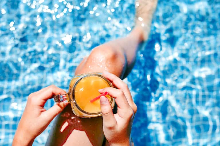Person holding tropical cocktail while relaxing in swimming pool