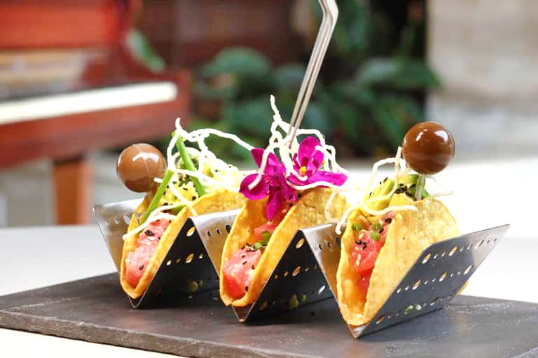Close-up of three gourmet tacos with vibrant toppings and garnish on a slate serving plate