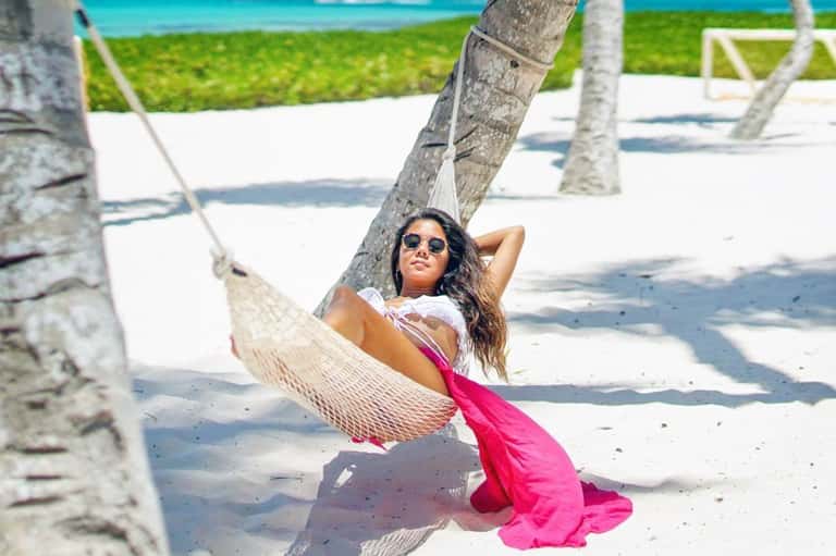 Woman relaxing in a hammock between palm trees on a white sand beach