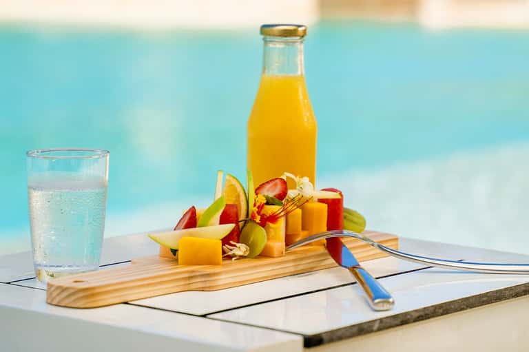 Colorful fruit platter with juice bottle by poolside, featuring fresh tropical fruits and sparkling water