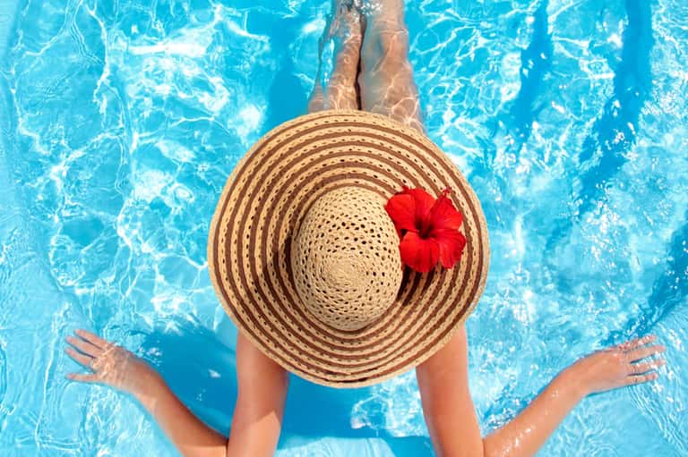 Woman floating in resort pool wearing wide-brimmed straw hat with red flower accent