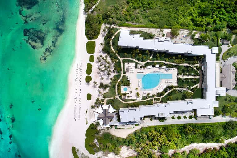 Aerial view of beachfront resort with pools, white building, and pristine turquoise ocean