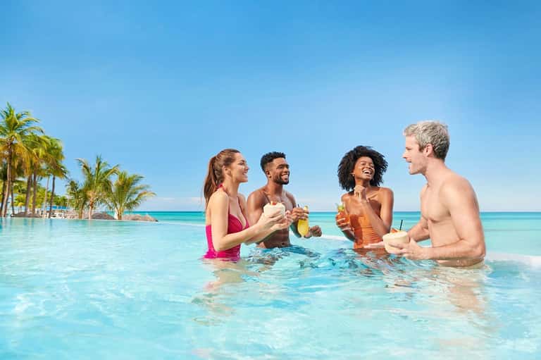Four people in turquoise infinity pool with palm trees and ocean horizon