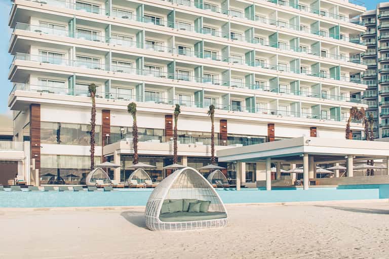 Beachfront hotel building with white pod-shaped lounger on sand and ocean view