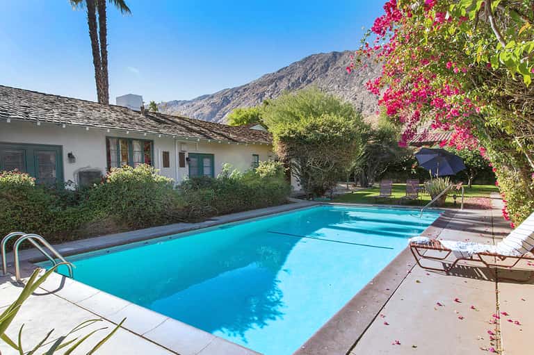 Resort pool nestled against mountains with blooming magenta bougainvillea and palm trees