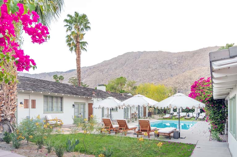 Desert resort with white cabanas, lounge chairs, pool, palm trees, and mountain backdrop