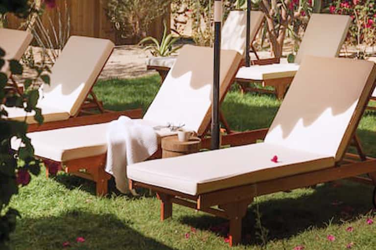 Wooden lounge chairs with white cushions arranged on manicured lawn surrounded by flowering plants