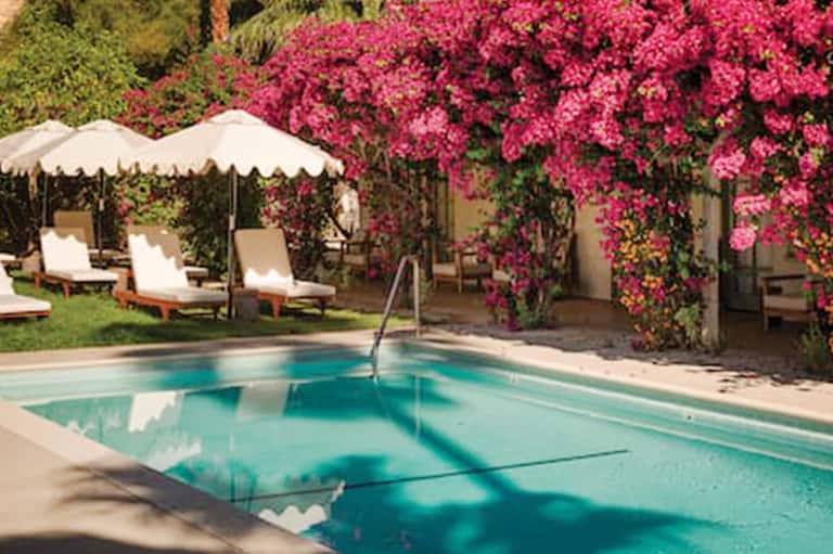 Resort pool with turquoise water, white umbrellas, lounge chairs, and vibrant pink bougainvillea flowers