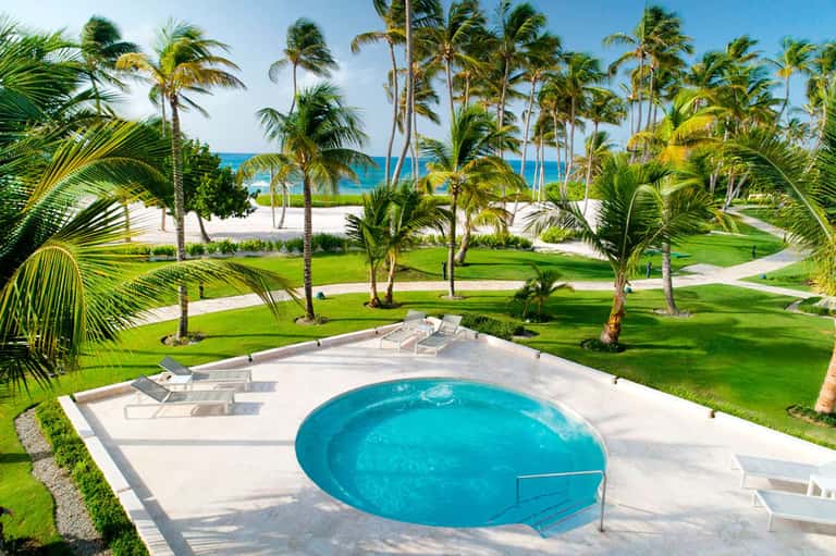 Beachfront resort with pool, palm trees, lounge chairs, and ocean beyond